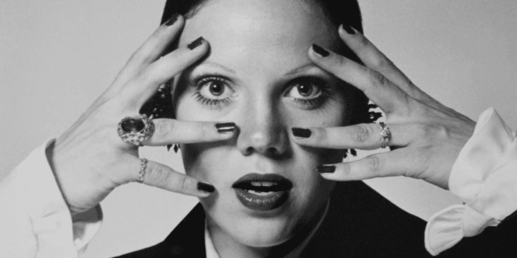 View of a woman with her hands and fingers sprawled out touching her face. her face looks shocked. Image is high fashion
